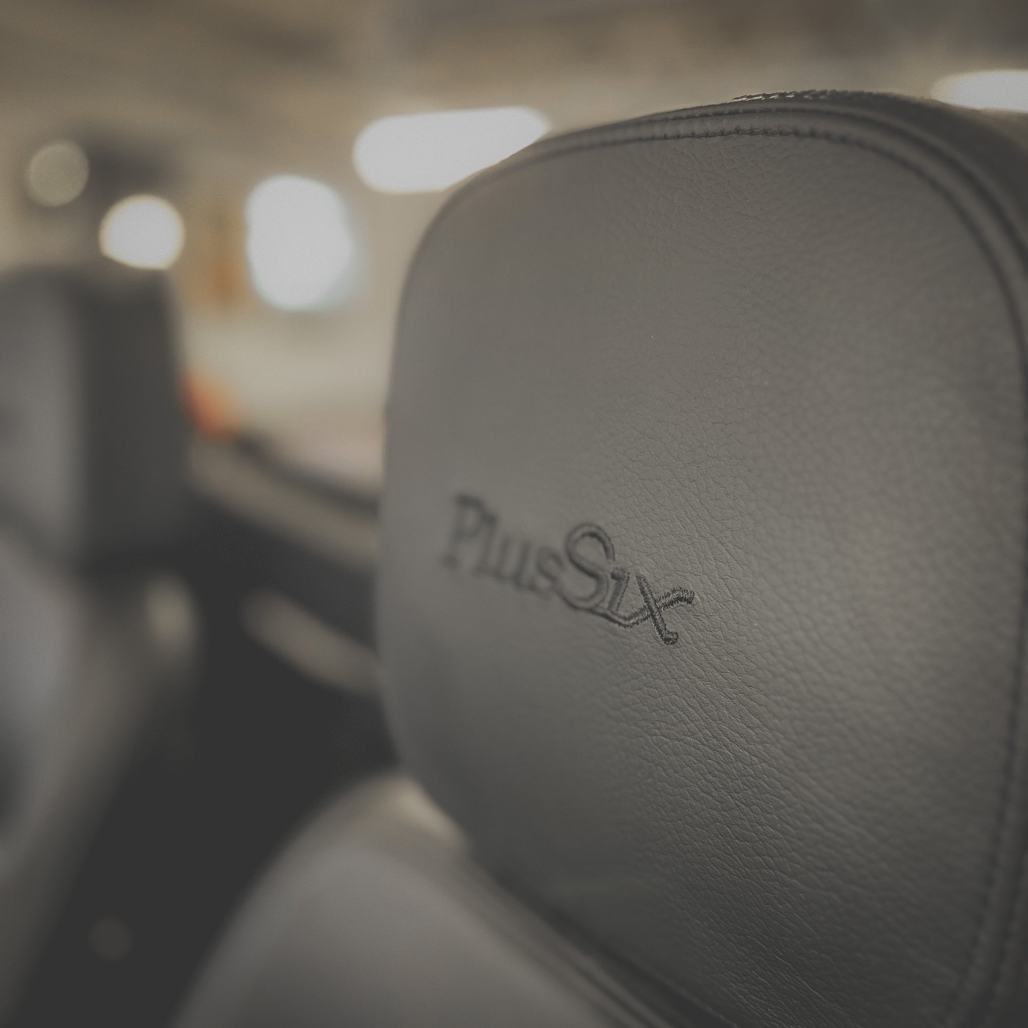 Close-up of a car seat with 'Plus Six' branding, blurred interior background