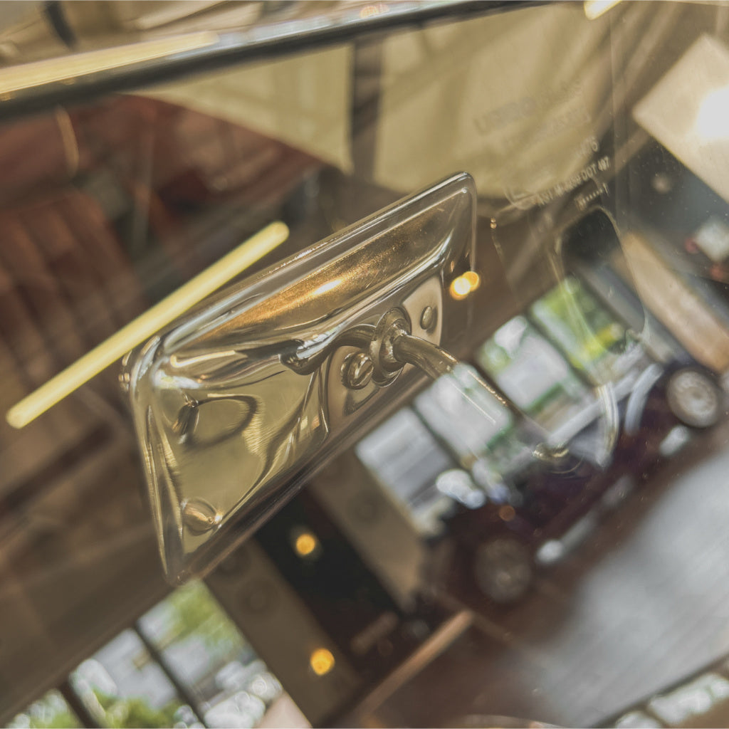 A close-up of a shiny chrome car door handle reflected in glass, with a blurred interior and outdoor scene visible behind it.