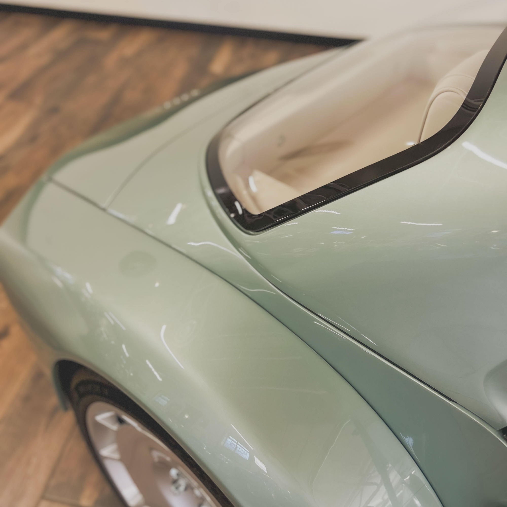 Close-up of a light green car with a wooden floor background