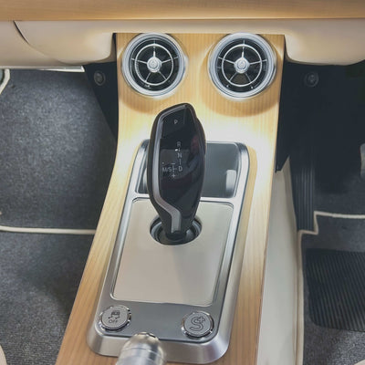Car gear shift lever with wooden panel and air vents in a vehicle interior.