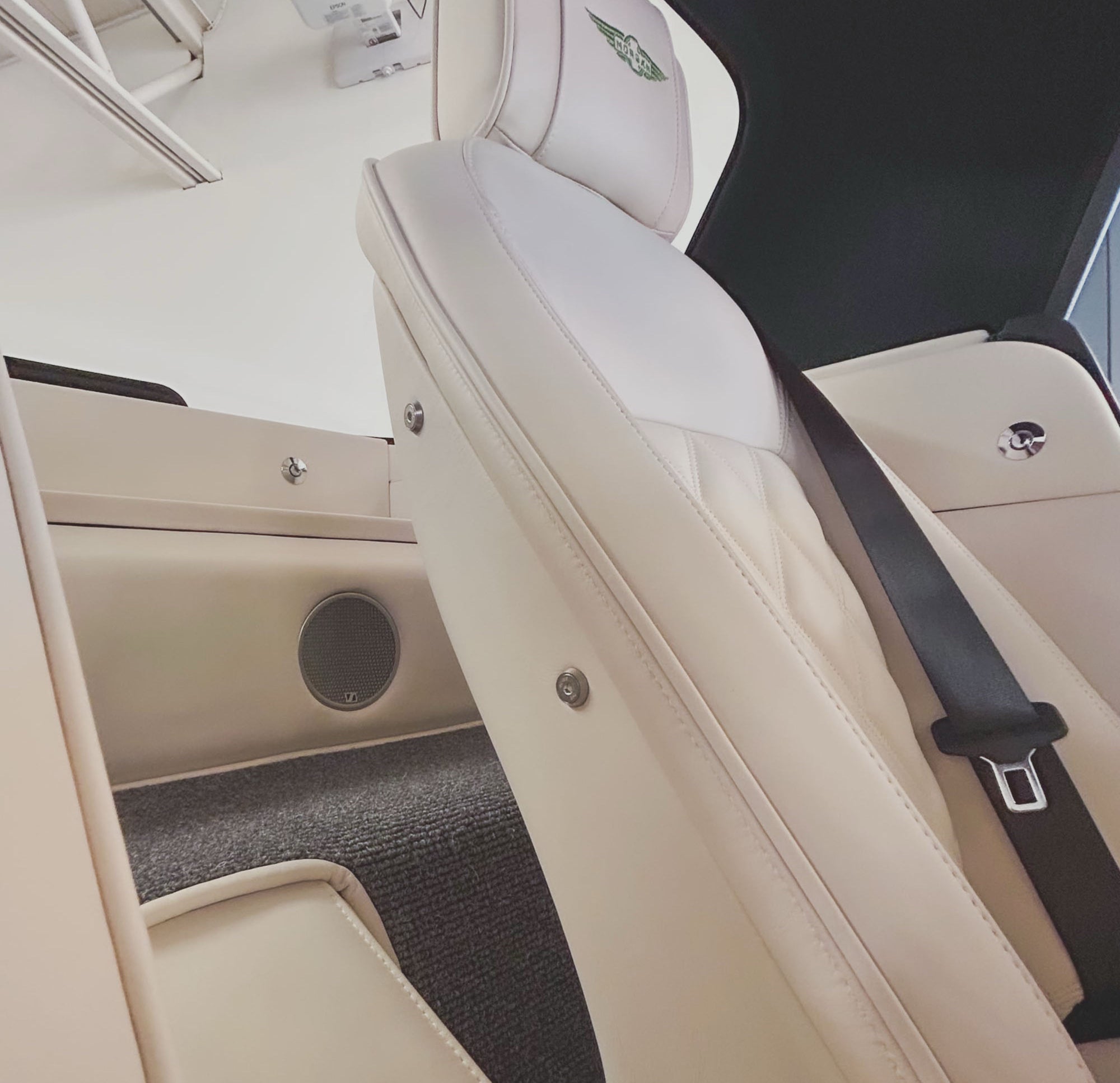 Close-up of a car's beige interior with a seat belt and speaker.