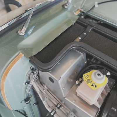 Close-up of a vehicle's open hood with mechanical components and a yellow warning label.