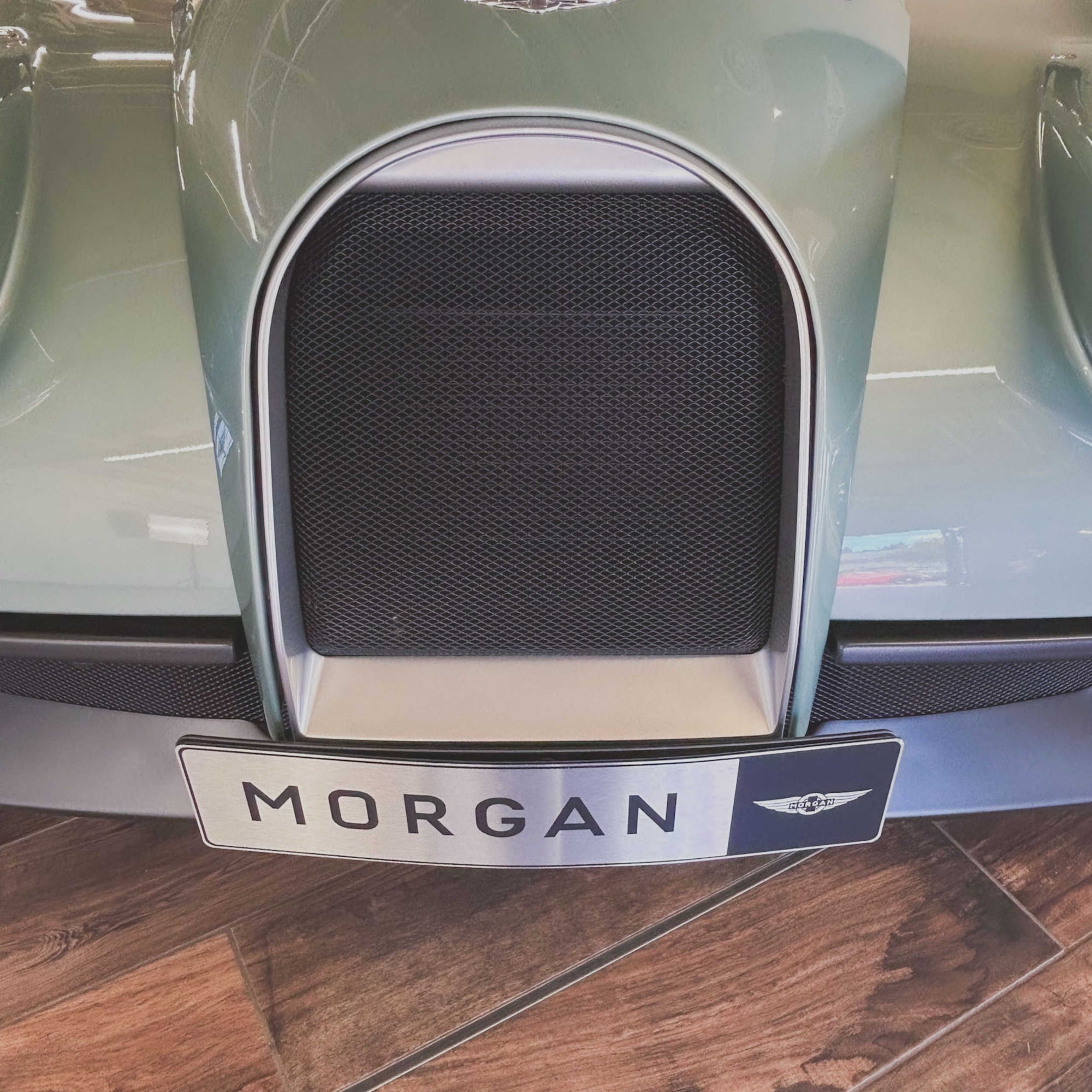 Close-up of a car grille with 'Morgan' branding on a wooden floor.
