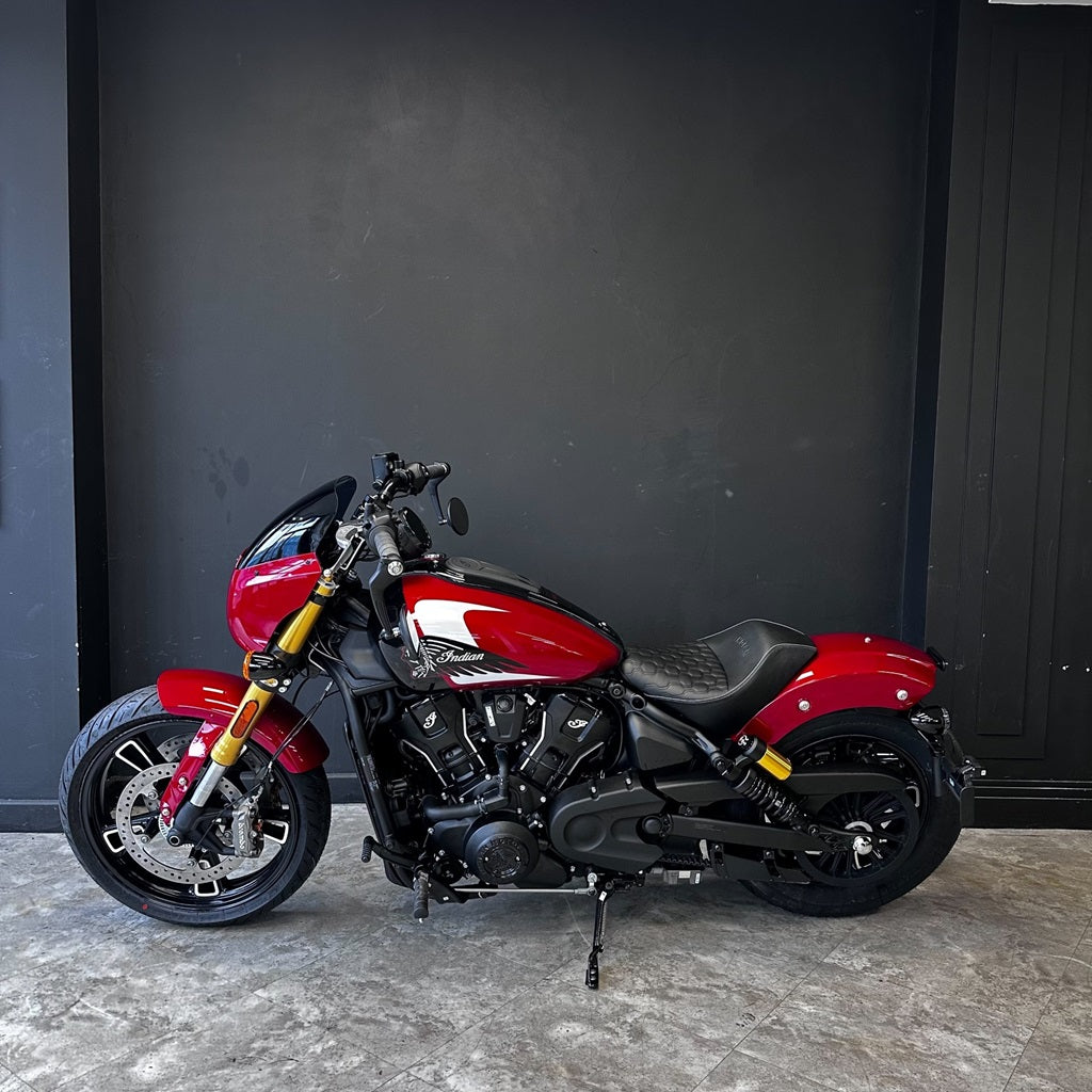 2025 Indian Scout 101 – SUNSET RED METALLIC WITH GRAPHICS- PRELOVED  Red motorcycle parked against a dark gray wall