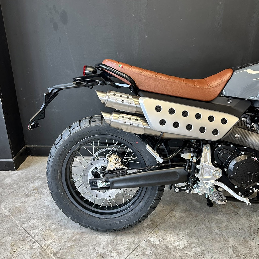Motorcycle with brown seat and black exhaust against a dark wall.