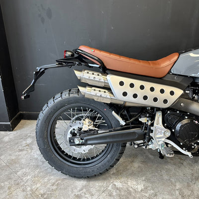 Motorcycle with brown seat and black exhaust against a dark wall.