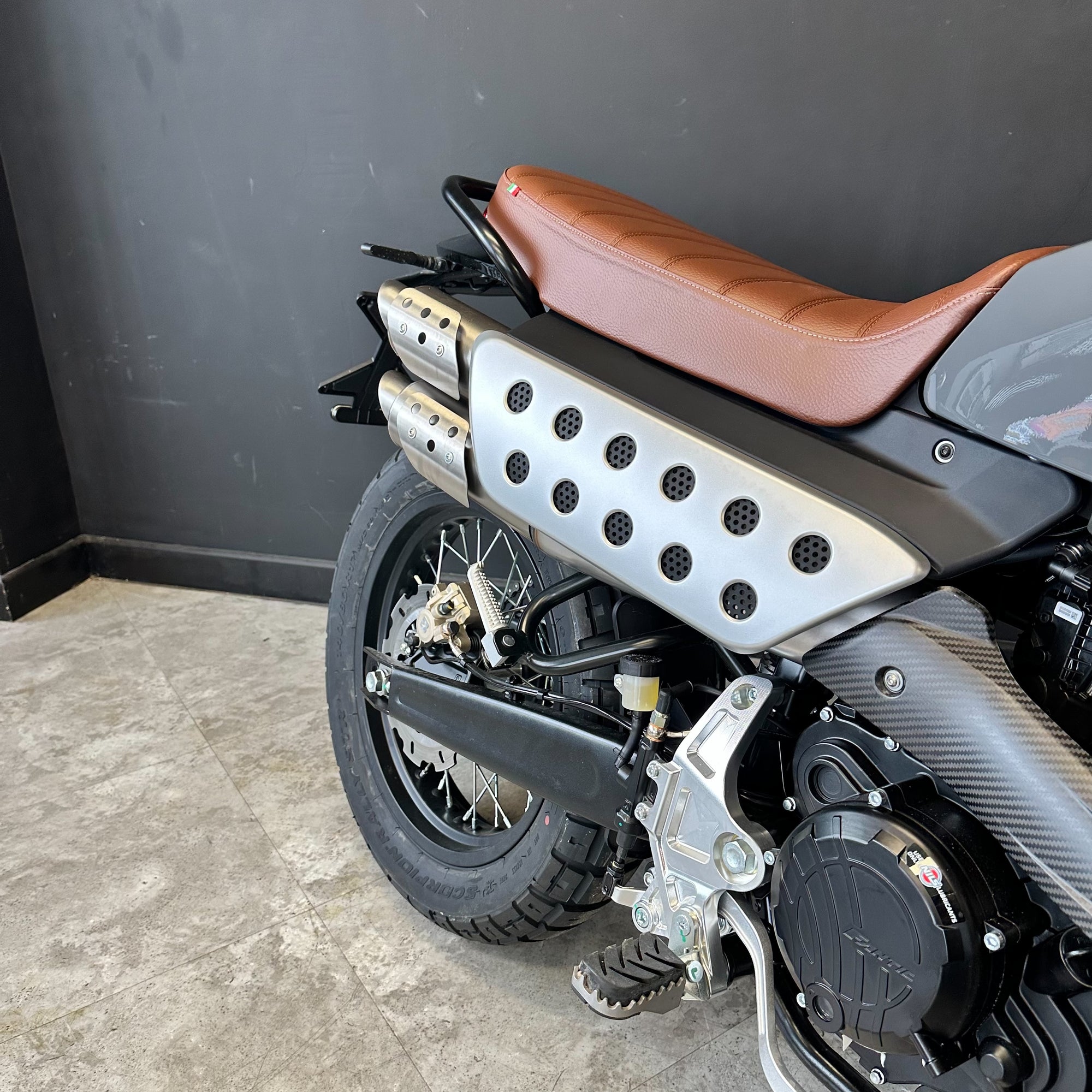 Motorcycle with brown seat and black exhaust on a gray floor against a dark wall