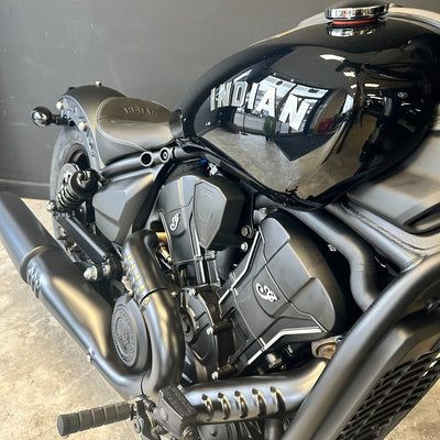 Close-up of a matte black and dark gray Indian motorcycle, showing the fuel tank, engine, exhaust, and seat against a dark gray indoor background.