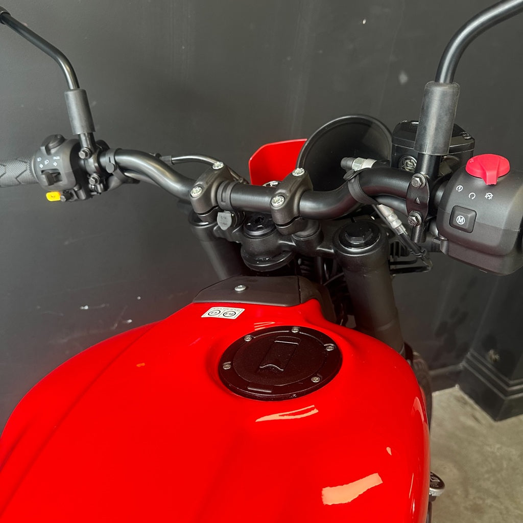Close-up of a red motorcycle tank and black handlebars against a dark gray background.