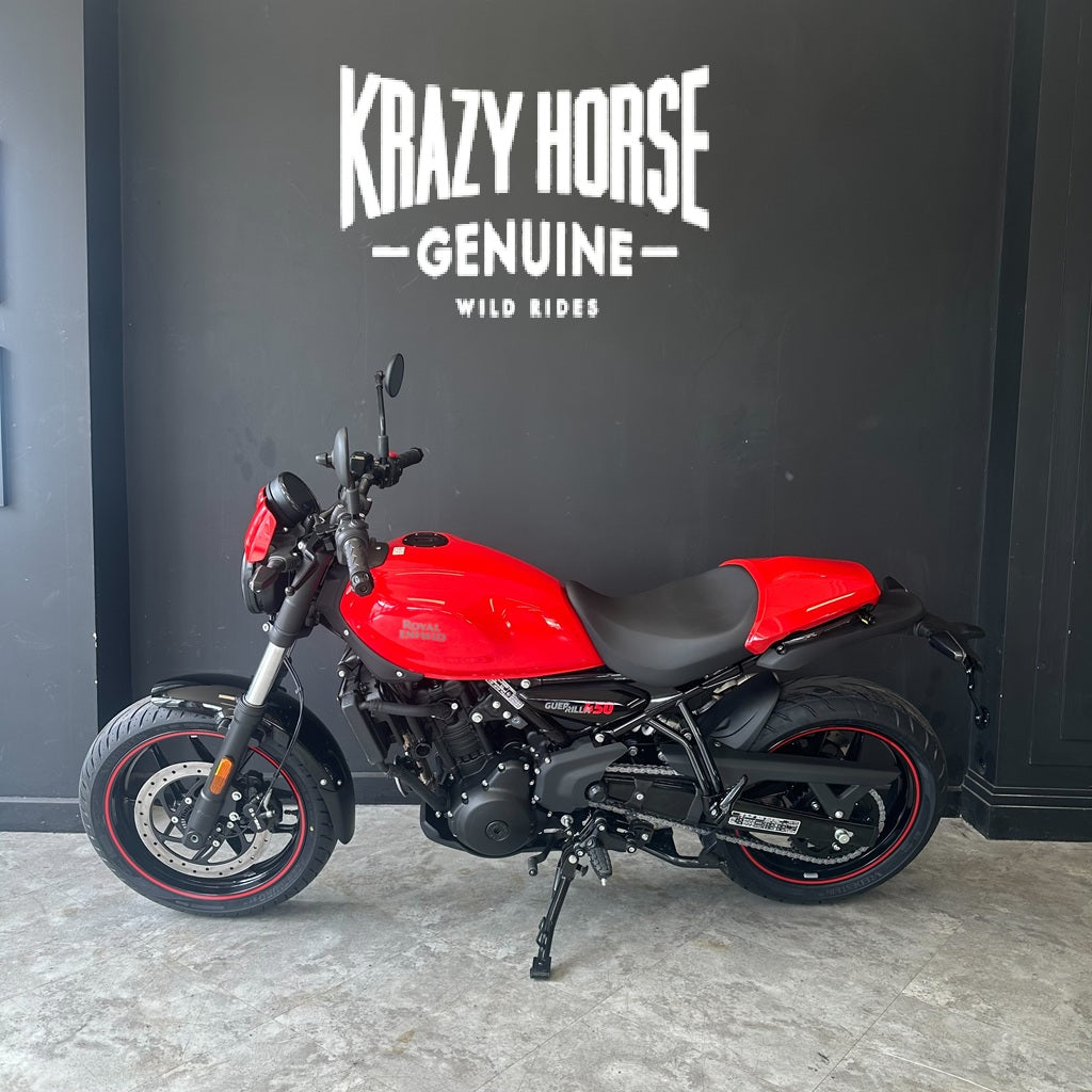 A red and black motorcycle parked indoors against a dark wall with the text 'Krazy Horse Genuine Wild Rides' above it.