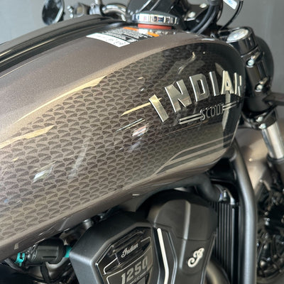Close-up of a motorcycle fuel tank with a metallic bronze finish, a subtle geometric pattern, and silver 'INDIAN SCOUT' branding.