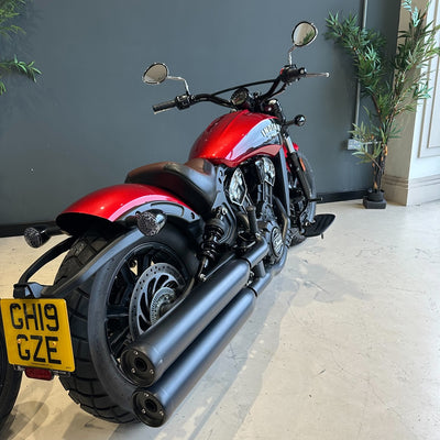 Red and black motorcycle indoors with a gray wall and plant in the background