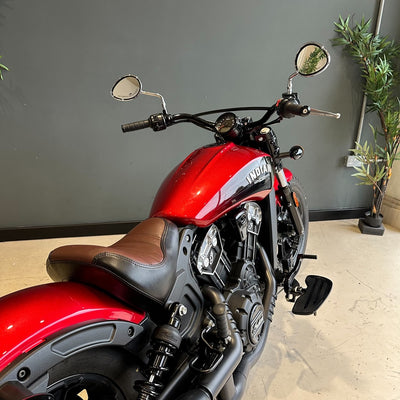 Red motorcycle with brown seat indoors against a gray wall