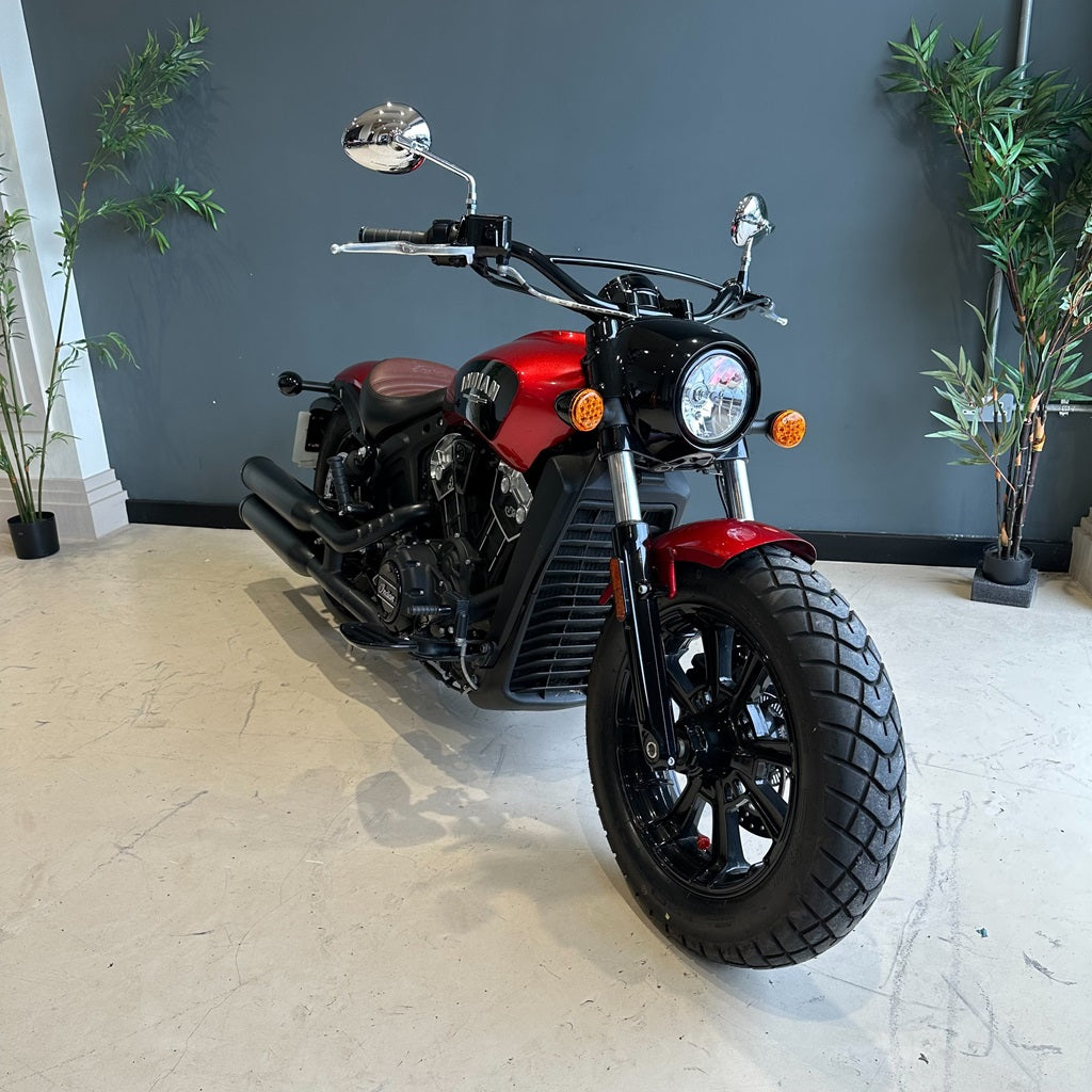 Red and black motorcycle indoors with a gray wall and plants in the background