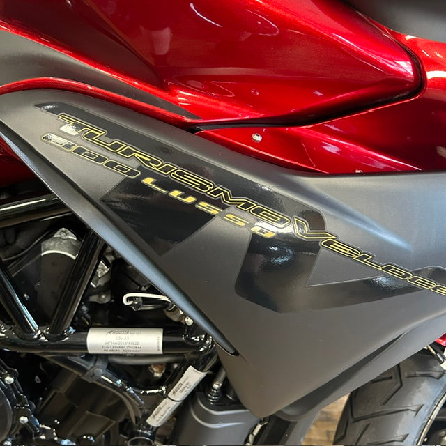 Close-up of a red and dark gray Yamaha Turismo Veloss 600 Lushi motorcycle body panel with gold lettering, showing the side fairing and engine components.