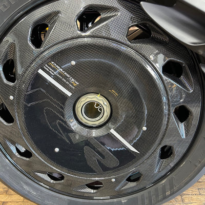 Close-up of a carbon fiber motorcycle wheel with a glossy black finish, featuring cutouts and a central hub.