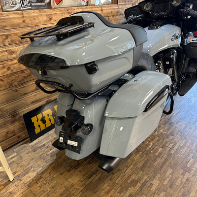 Gray motorcycle with saddlebags on a wooden floor, with a wooden wall and KR logo in the background.