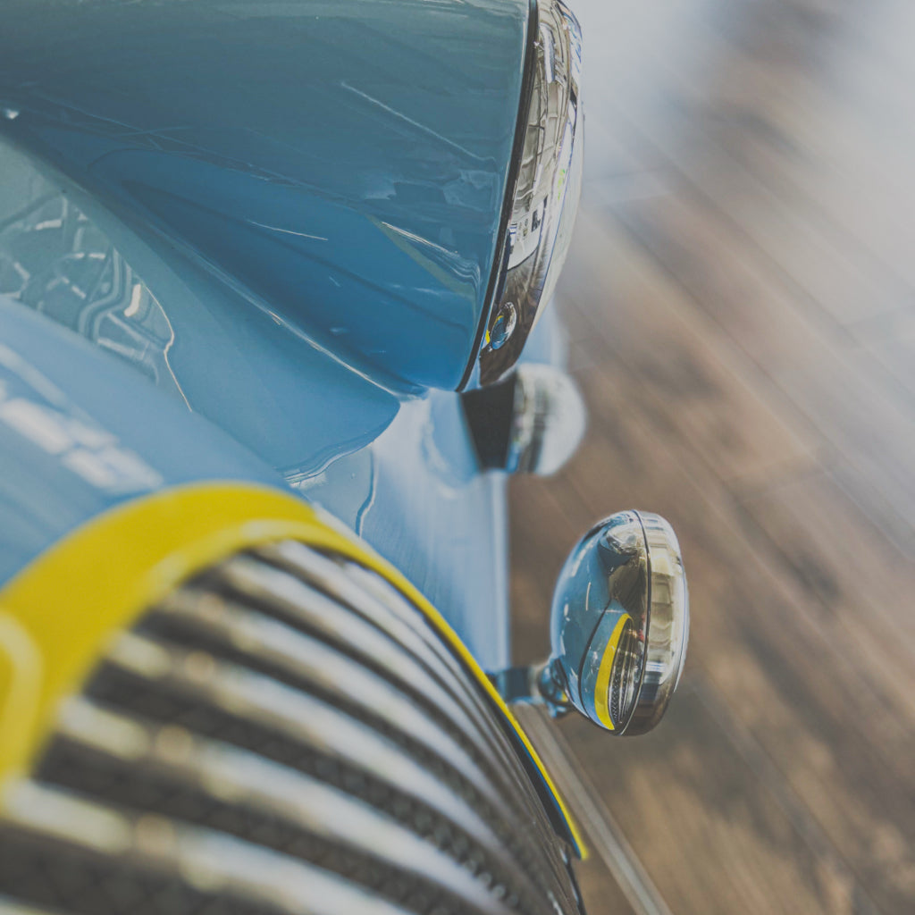 Close-up of a car's headlight and side mirror with a blurred background