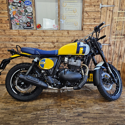 Motorcycle with yellow and blue accents leaning against a wooden wall.