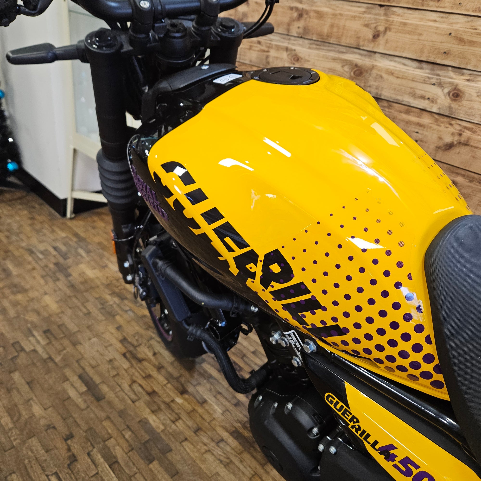Yellow motorcycle fuel tank with 'Guzzi' branding on a wooden floor.