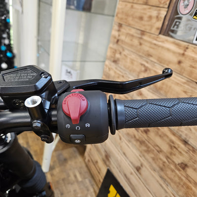 Close-up of a motorcycle handlebar with grip and control buttons on a wooden floor background