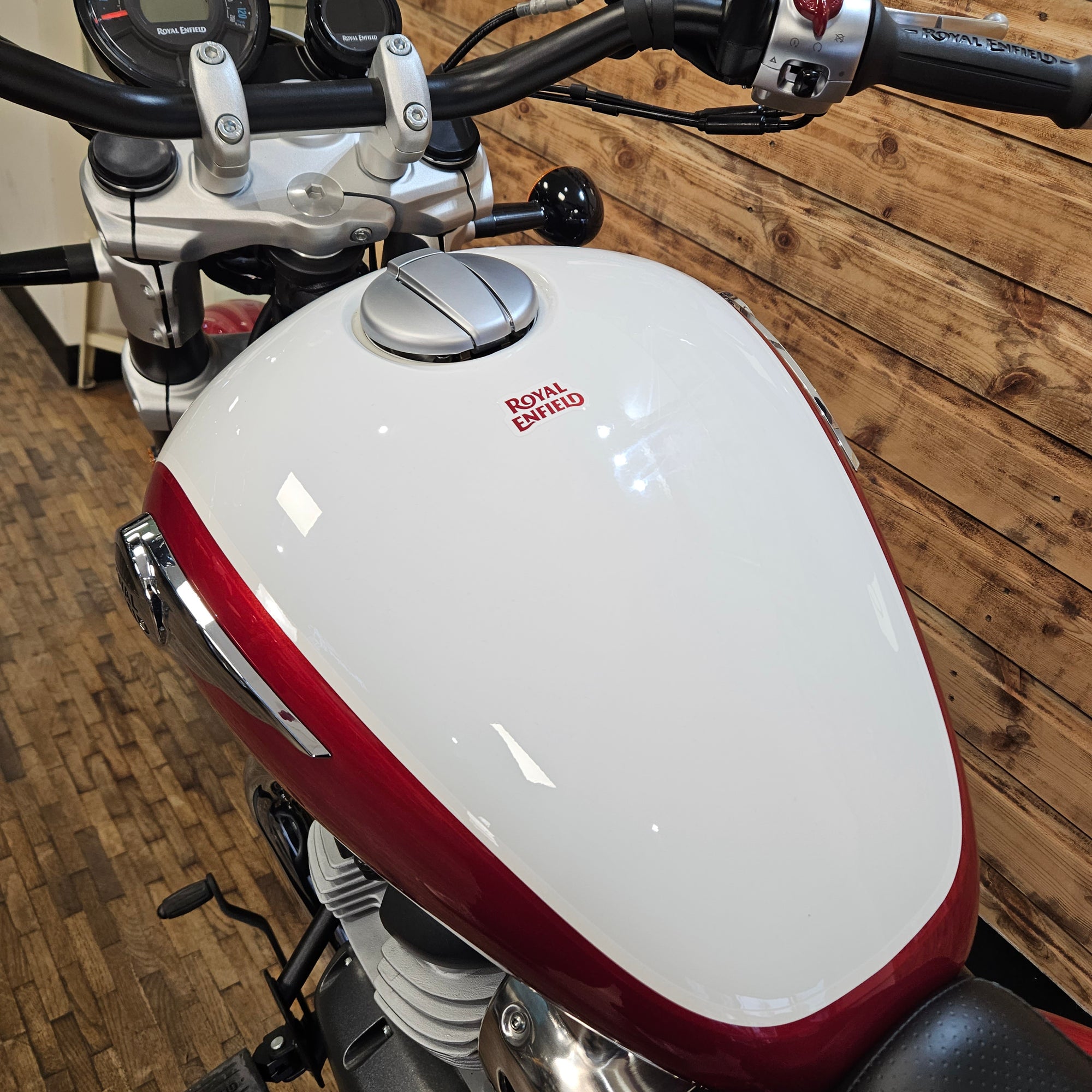 Close-up of a motorcycle's white and red fuel tank on a wooden floor.