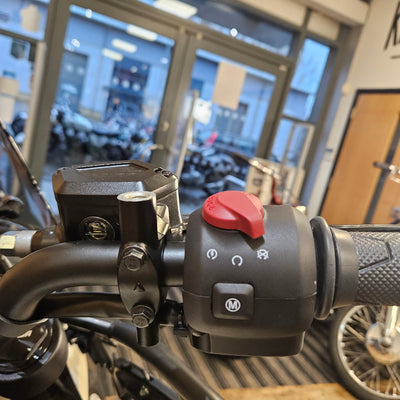 Close-up of a motorcycle handlebar with controls and a blurred indoor background