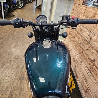 Close-up of a motorcycle's handlebar and front section against a wooden wall.