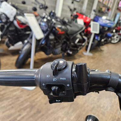Close-up of a motorcycle handlebar with control buttons, blurred background of motorcycles.