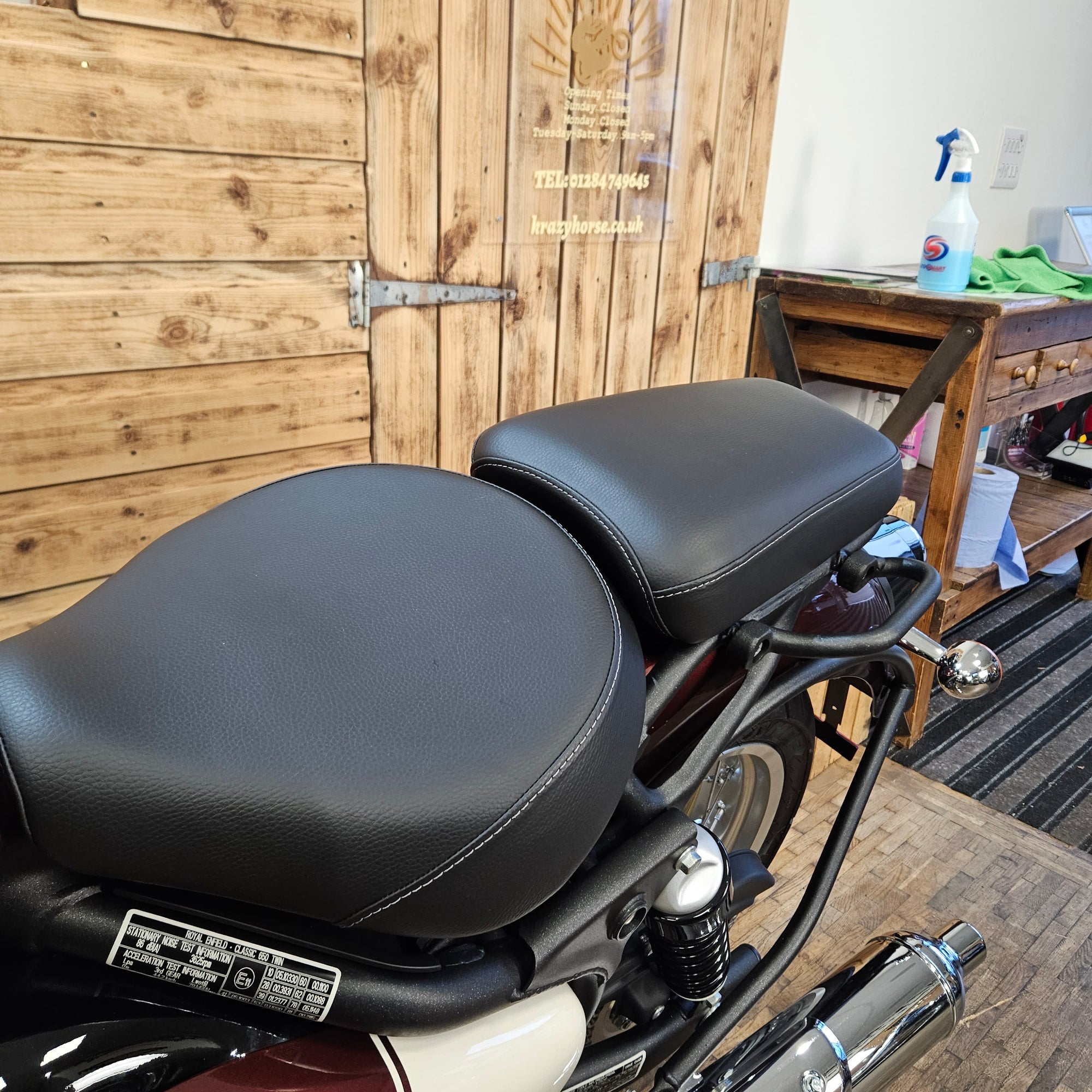 Motorcycle seat on a wooden deck with a bench and cleaning supplies in the background