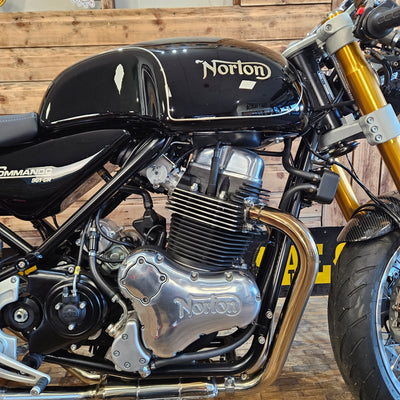 Close-up of a Norton motorcycle engine and exhaust system against a wooden background