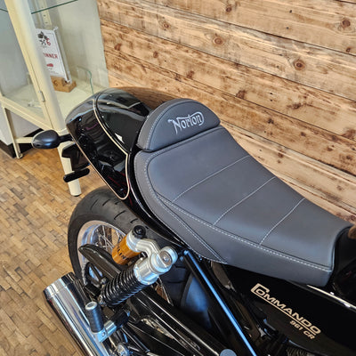 Gray motorcycle seat with 'Norton' branding on a wooden floor.