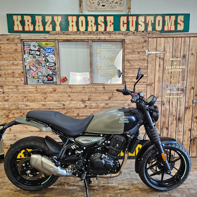 Motorcycle leaning against a wooden wall with 'Krazy Horse Customs' sign.