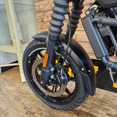Close-up of a motorcycle wheel and suspension on a wooden floor.