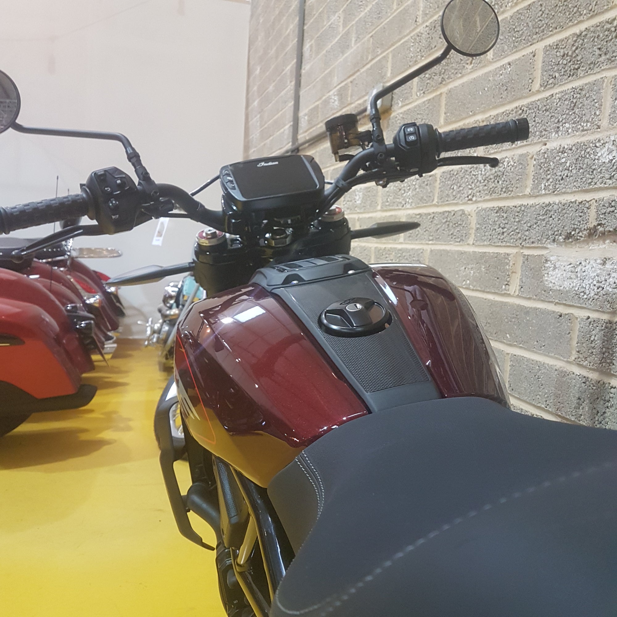 Close-up of a motorcycle's handlebar and front section against a tiled wall.