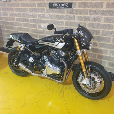 Black Norton motorcycle parked against a brick wall.