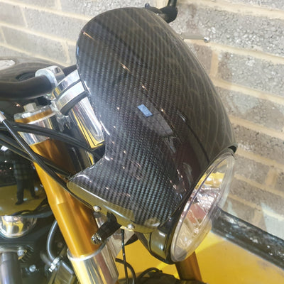 Close-up of a motorcycle headlight with carbon fiber cover on a blurred background