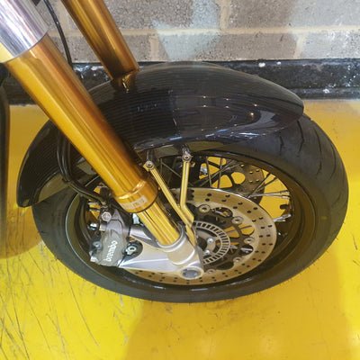 Norton Commando 961 Street - Black - PreLoved Close-up of a motorcycle wheel with gold suspension fork on a yellow surface.