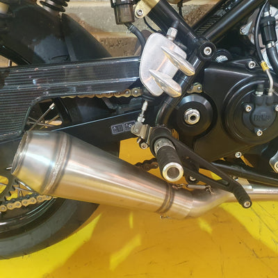 Close-up of a motorcycle exhaust and chain on a yellow surface