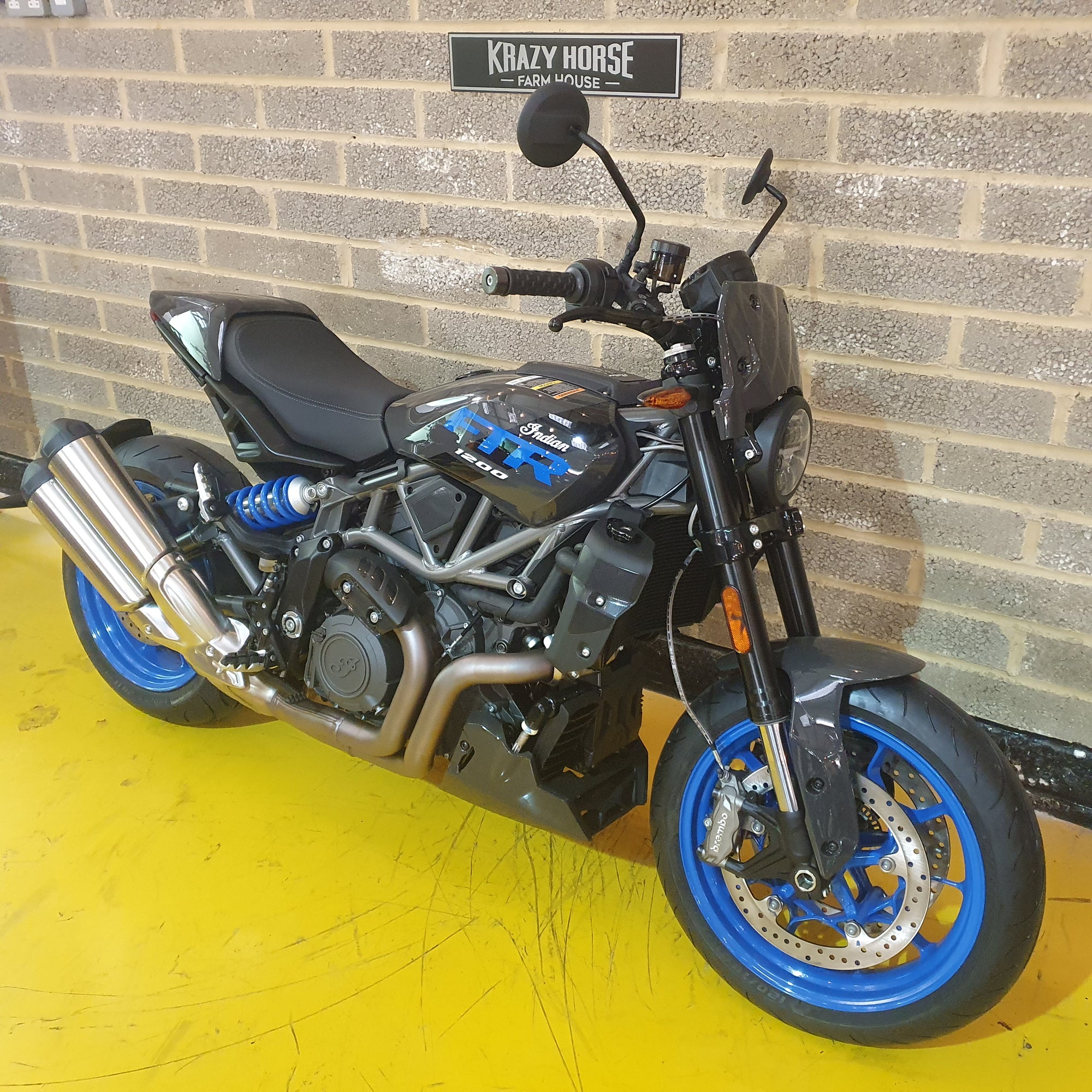 Indian FTR Motorcycle with blue wheels parked against a brick wall.