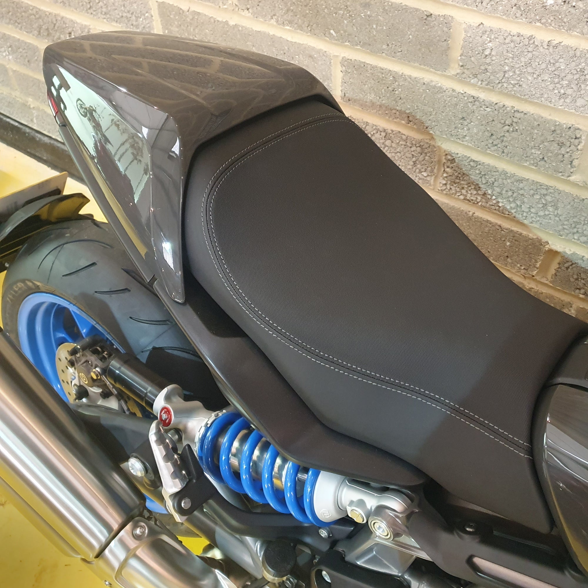 Close-up of a Indian FTR motorcycle seat and suspension system against a brick wall.