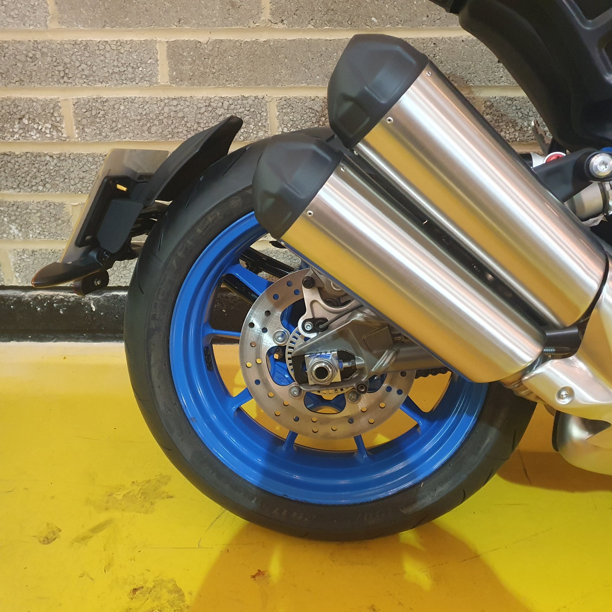 Close-up of a Indian FTR motorcycle wheel with a metal exhaust pipe against a brick wall.