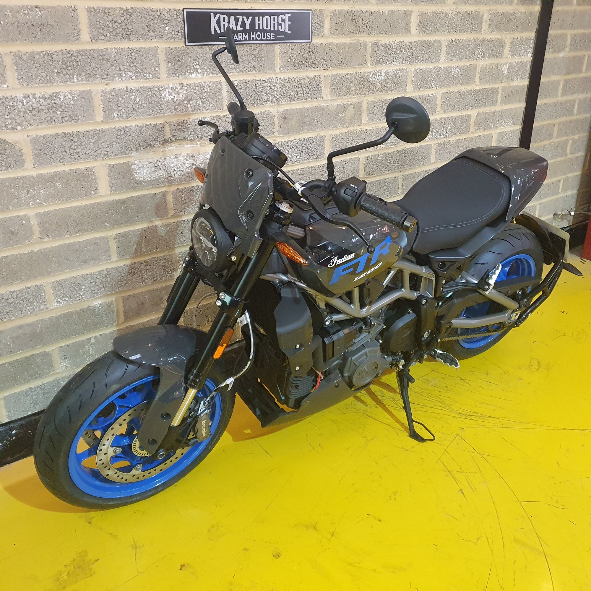 Motorcycle with blue wheels parked against a brick wall.
