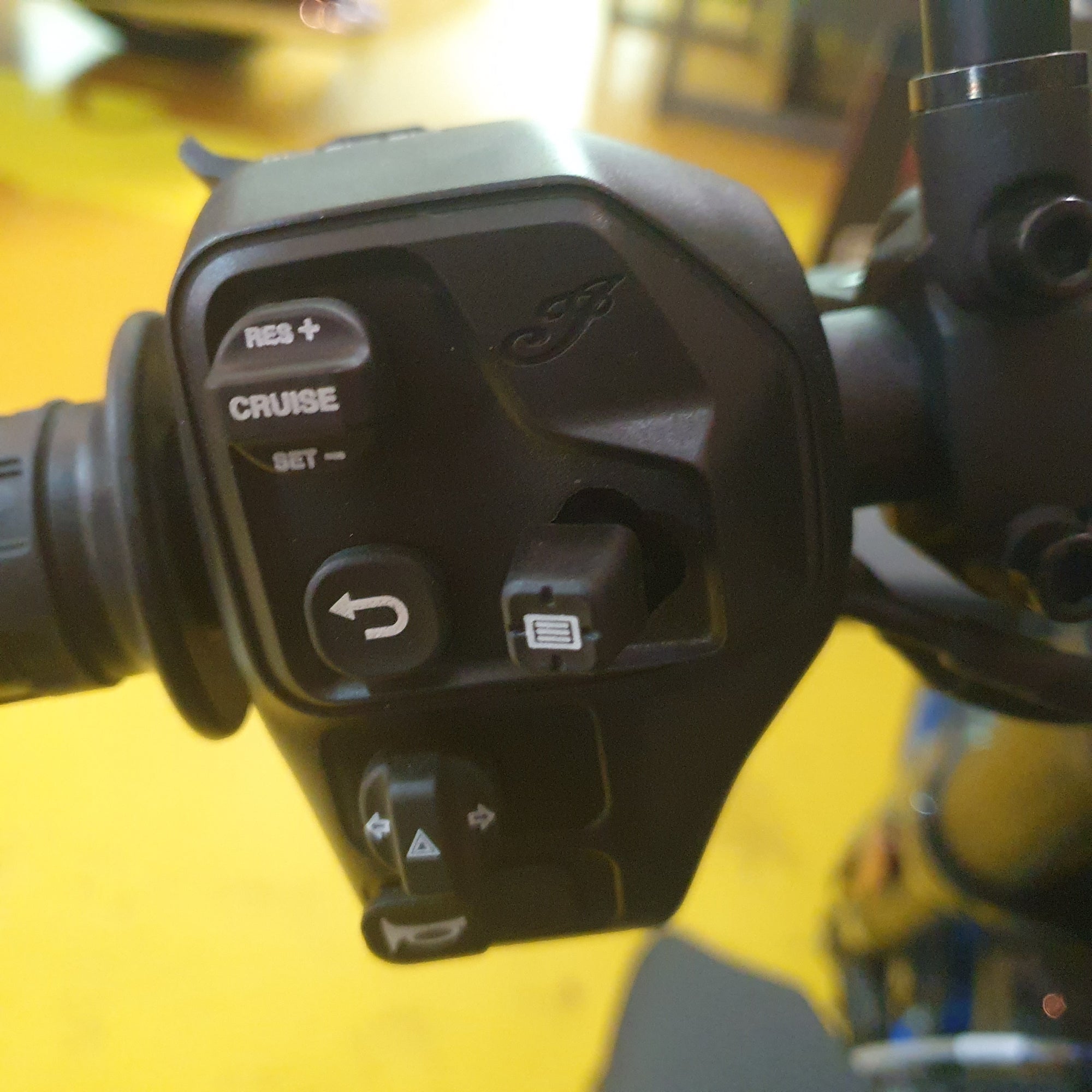 Close-up of a motorcycle handlebar control panel with cruise control buttons.
