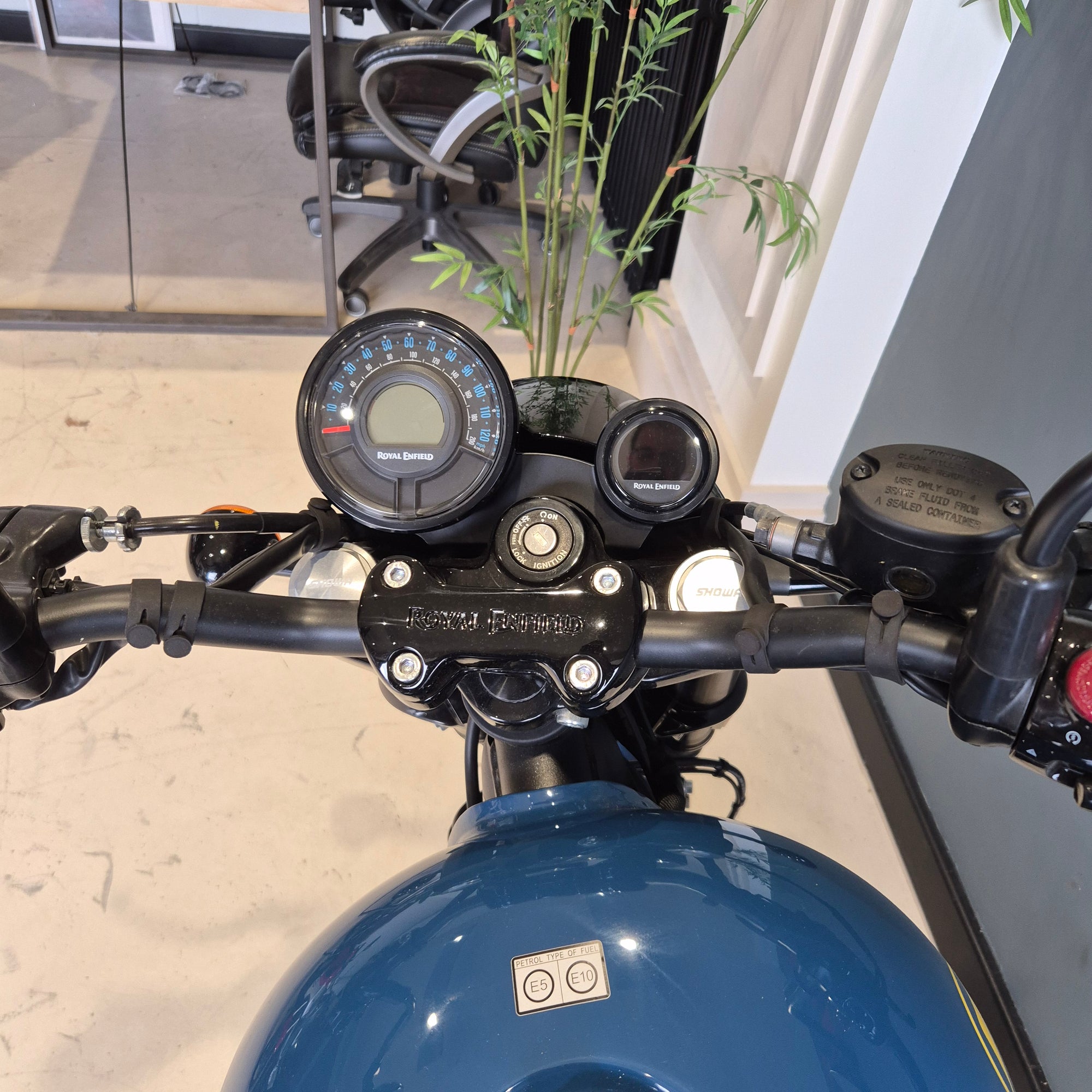 Close-up of a motorcycle's handlebar and dashboard with a blurred indoor background