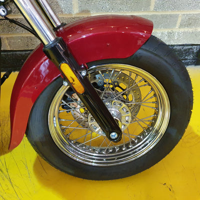 Close-up of a motorcycle wheel with red fender on a yellow surface.