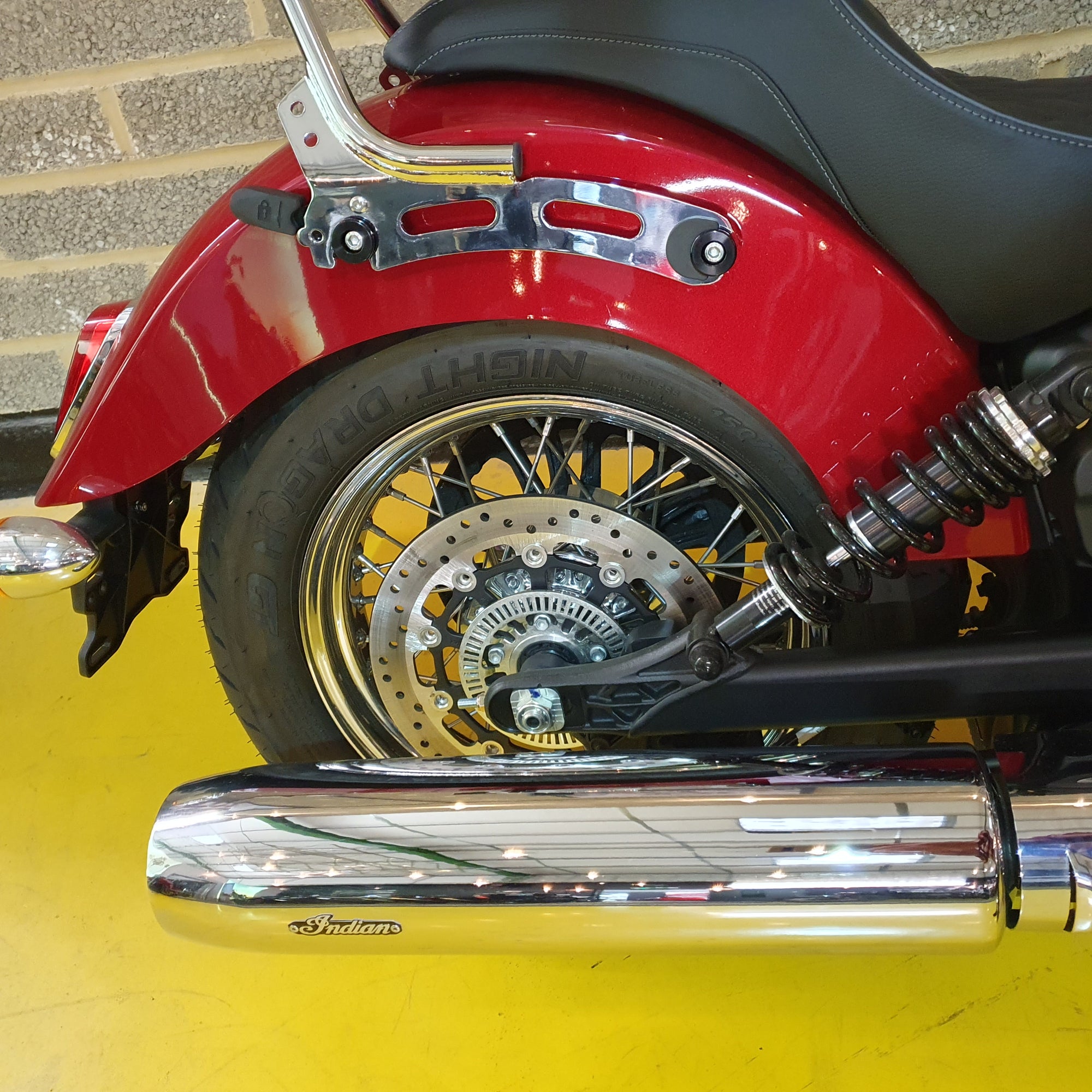 Close-up of a red motorcycle's rear wheel and suspension on a yellow floor.
