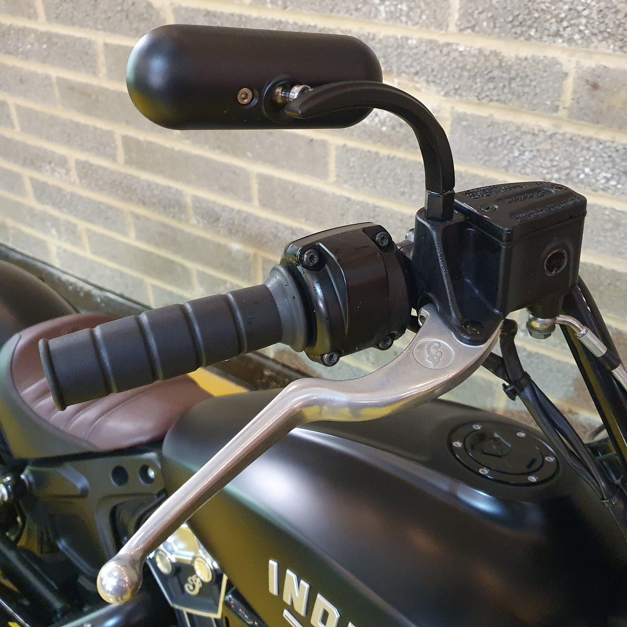 Close-up of a motorcycle handlebar with brake lever against a brick wall.