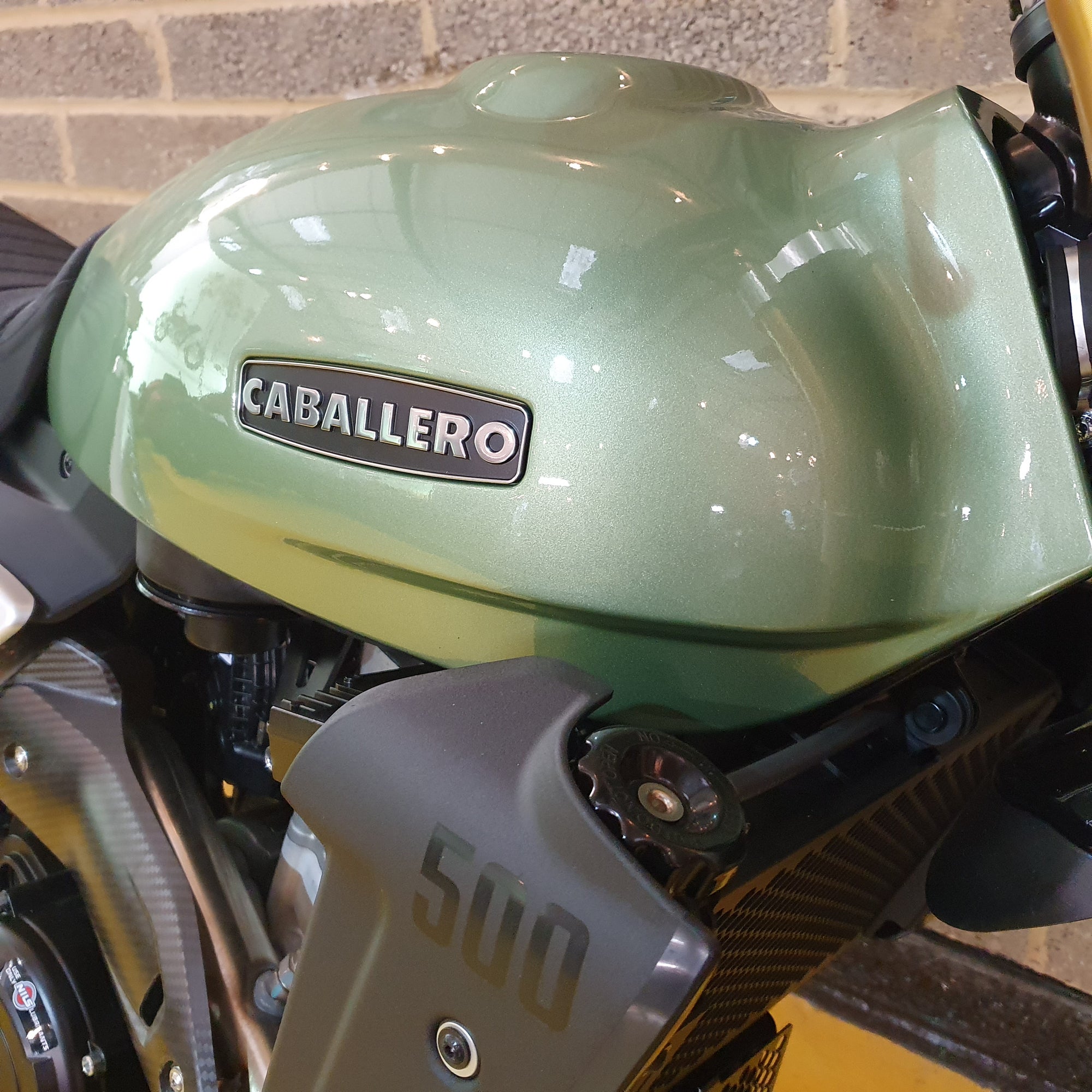 Close-up of a green motorcycle with 'Caballero' branding on a brick wall background.