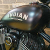 Close-up of a motorcycle fuel tank with 'Indian Chief' branding against a brick wall.